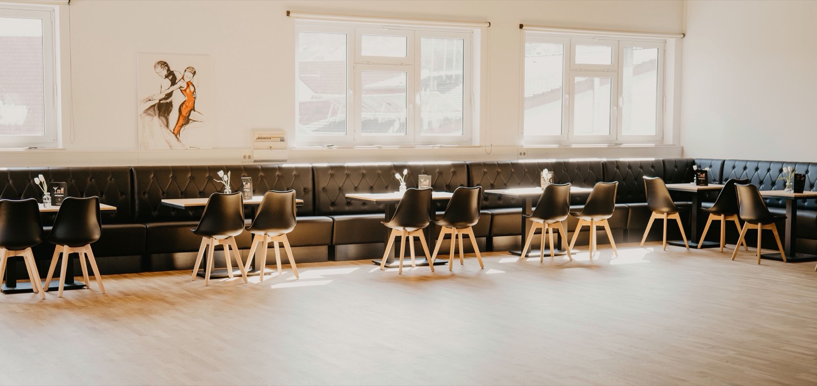 Der helle Saal mit Sitzbänken und Tanzbildern
